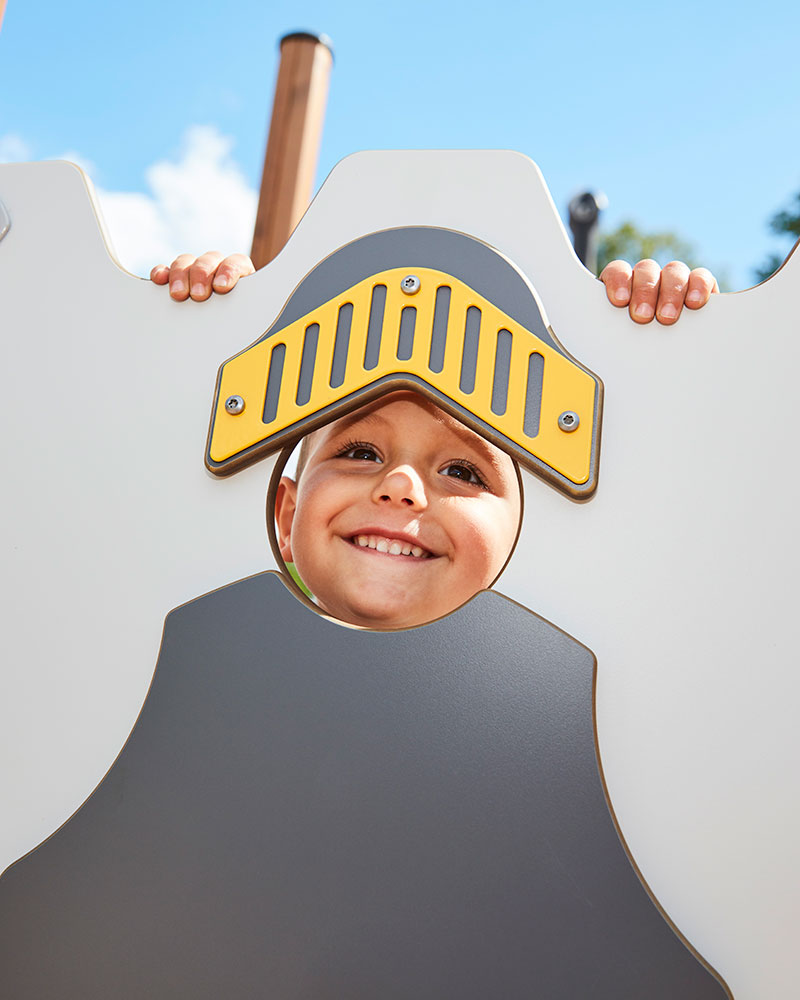 A young boy is looking through a telescope on top of a large wooden playground unit.